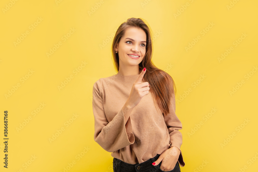 Pointing. Portrait of young caucasian woman isolated on yellow studio background with copyspace. Beautiful female model. Concept of human emotions, facial expression, sales, advertising, youth. Pointing. Portrait of young caucasian woman isolated on yellow studio background with copyspace. Beautiful female model. Concept of human emotions, facial expression, sales, advertising, youth.