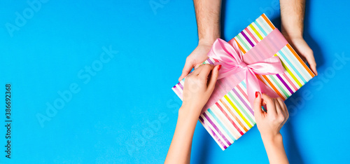 Top view of giving a present to a lovely person on colorful background. Couple congratulate each other. Festive concept. Copy space