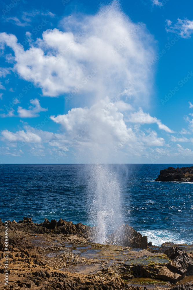 Geyser d'eau sortant d'un trou dans la caye  sur le littoral avec la mer bleu intense et un ciel dégagé avec quelques nuages