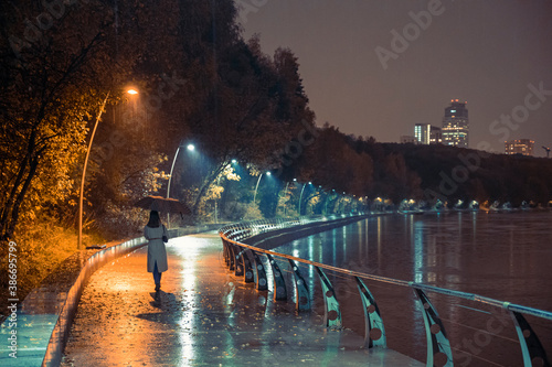 Girl with umbrella at night on the embankment in a heavy downpour