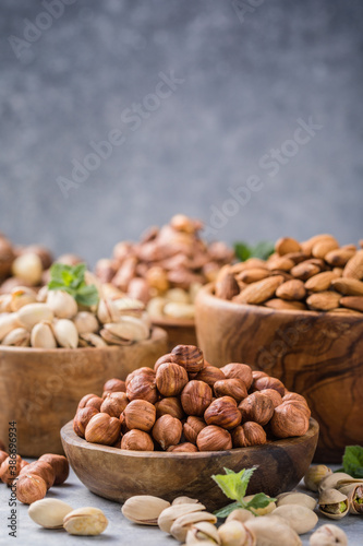 Assortment of nuts in a wooden bowls, on a gray background. Hazelnuts, pistachios, almonds, brazil nut, cashews