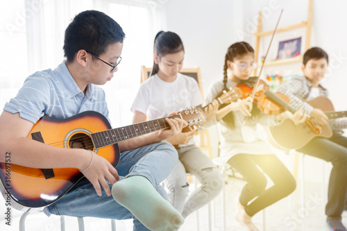 light and blur people, asian children sitting and playing guitar, asian children group playing music with acoustic musical instrument, they feeling fun and happy in training time, music education
