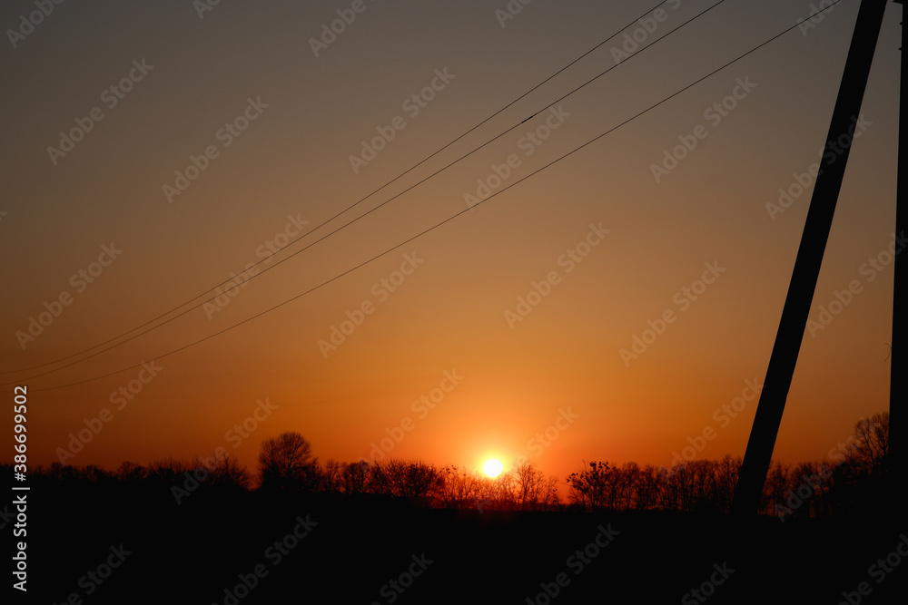 High voltage electric pylon and electrical wire with sunset sky.