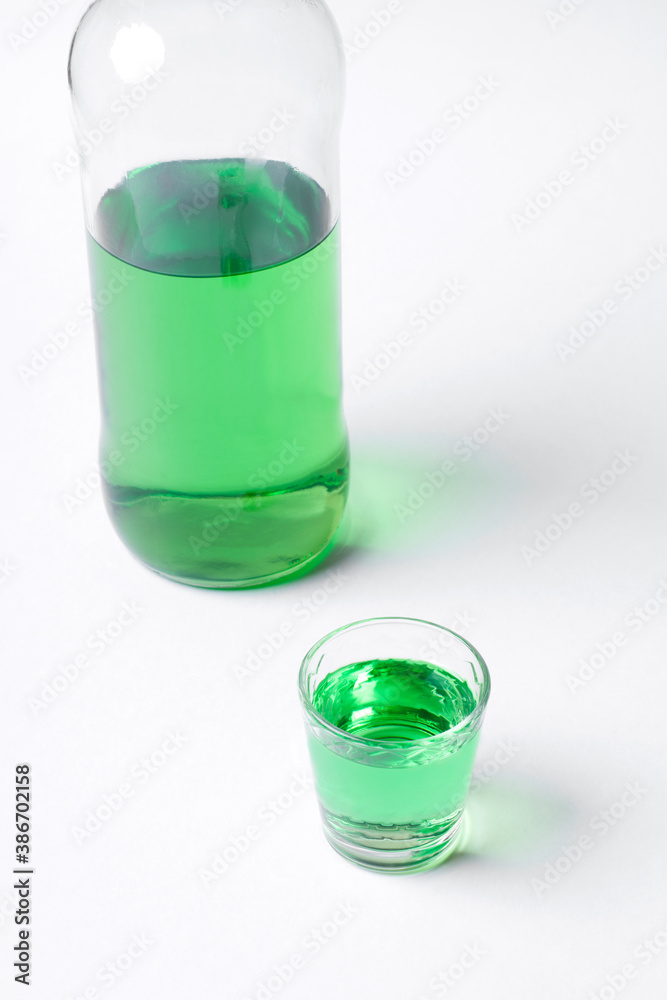 Green liquor in a shot glass and bottle on the white table Green liquor in a shot glass and bottle on the white table