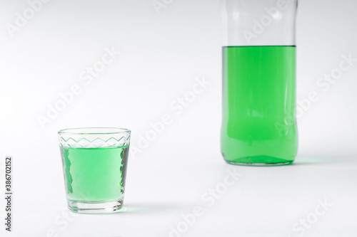 Green liquor in a shot glass and bottle on the white table photo