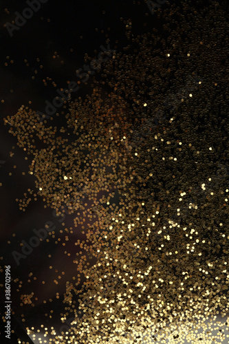 Gold (bronze) glitter shine dots confetti on black. Abstract light blink sparkle backgound.