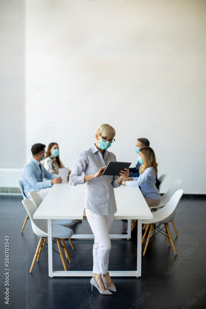 Mature businesswoman with protective mask using digital tablet in office Mature businesswoman with protective mask using digital tablet in office