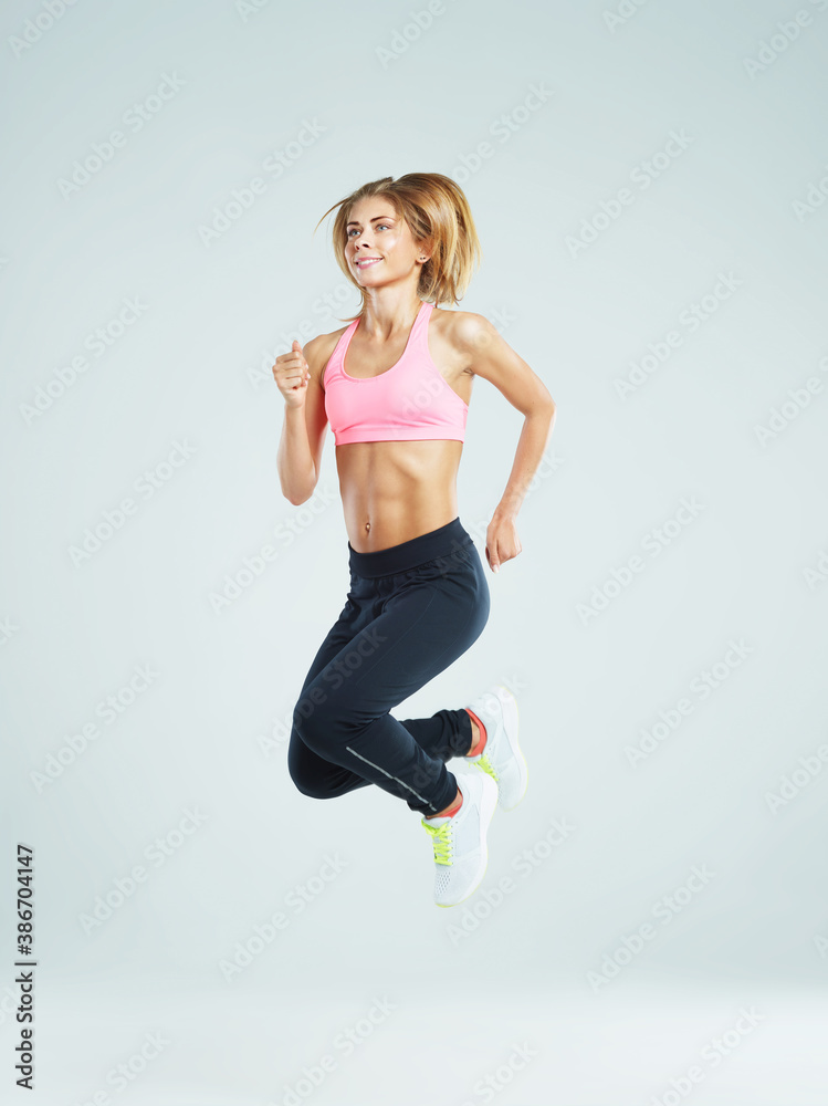 Side view of smiling fit young woman in crop top jumping up in air against white studio background