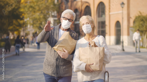 Senior couple in safety mask walking along city street with shopping bags
