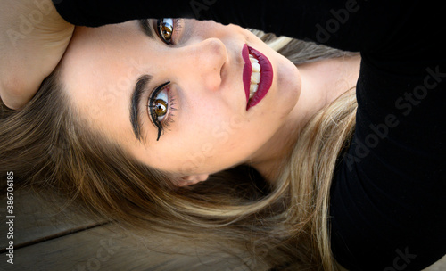 Retrato primer plano de la cara de una mujer joven rubia con el brazo por encima de la cabeza, labios pintados de rojo ojos marrones y sonrisa, piel blanca en horizontal apaisado. photo