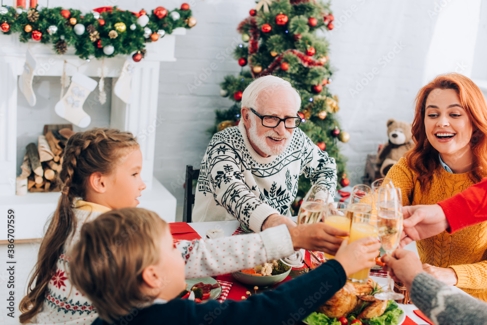 Happy family toasting, sitting at festive table near fireside and Christmas pine - obrazy, fototapety, plakaty 