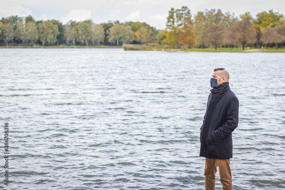 A man in a mask stands in the park at a lake A man in a mask stands in the park at a lake
