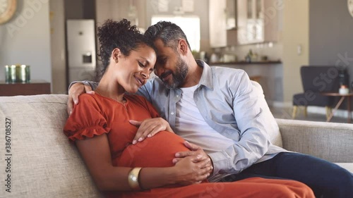 Mid adult couple expecting a baby while husband caresses the belly of his pregnant african woman. Happy father hands on expecting mother's baby bump while embracing her on couch.