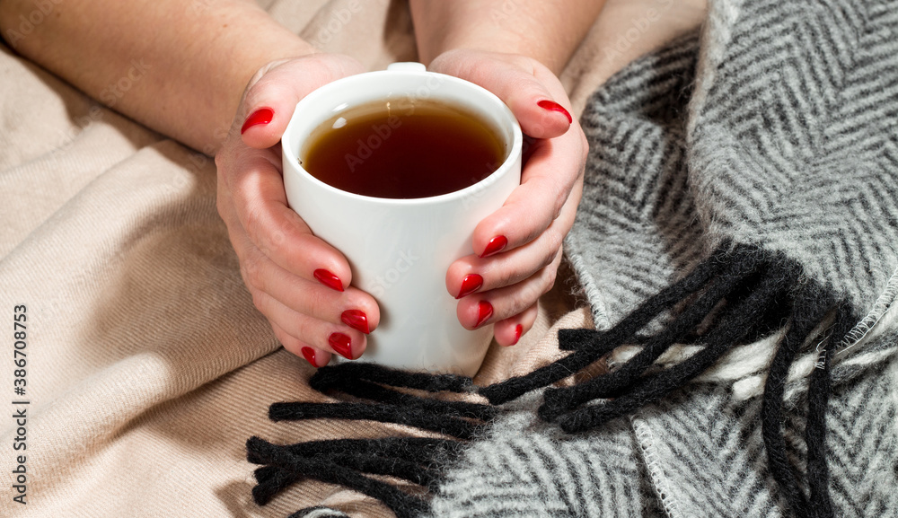 Woman hands with red manicure holding a cup of hot tea or coffee. Wool blankets. Winter coziness concept