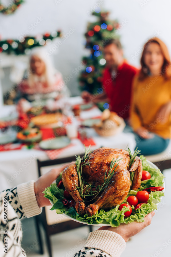 Fototapeta premium senior man holding delicious roasted turkey near family sitting at festive table