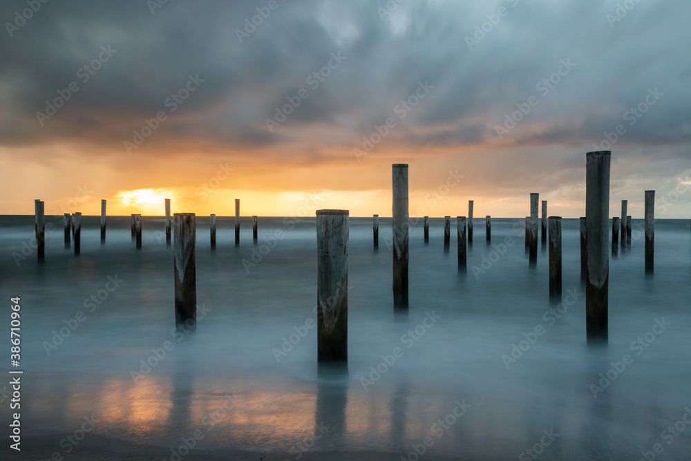 LONG EXPOSURE PHOTOGRAPHY, taken at the North Sea in Petten with the pole village in the sea, taken during the evening hours with a beautiful setting orange sun and heavy clouds.