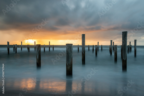 LONG EXPOSURE PHOTOGRAPHY, taken at the North Sea in Petten with the pole village in the sea, taken during the evening hours with a beautiful setting orange sun and heavy clouds.