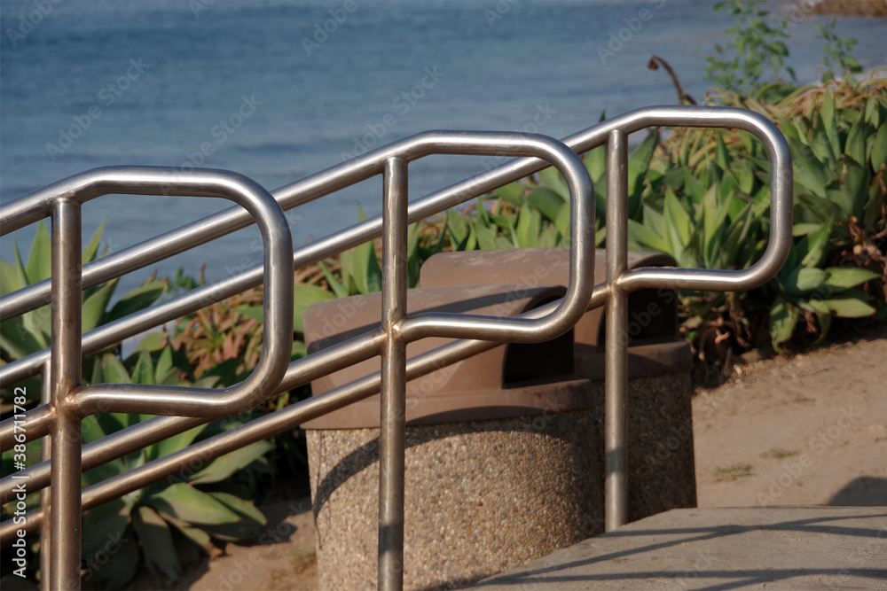 Three stainless steel handrails at stairs to an ocean beach