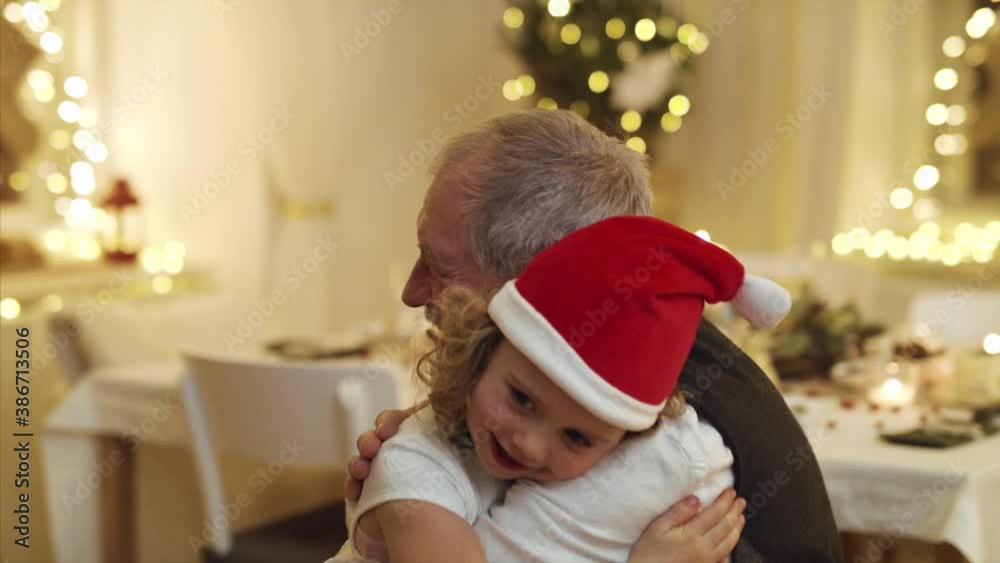 Small girl with senior grandfather indoors at home at Christmas, hugging.