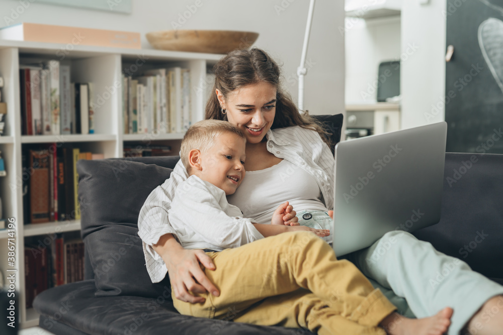 single mother with her child laying on sofa and using computer at home single mother with her child laying on sofa and using computer at home