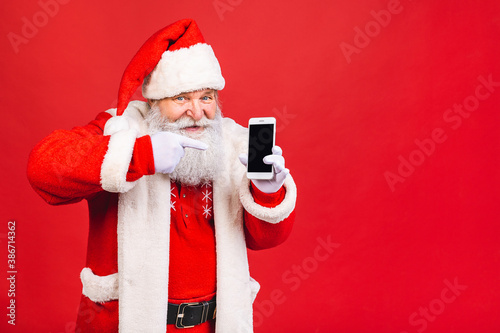 Portrait of nice attractive handsome amazed Santa using phone gadget 5g fast speed blog blogger browsing multimedia isolated over red background.