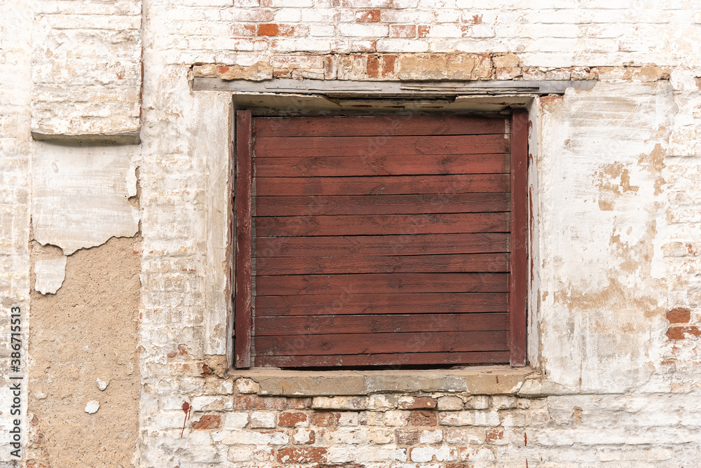Old window with brown wooden shatter on wall of abandoned building made with red bricks covered with white stucco on city street. Traditional architectural style
