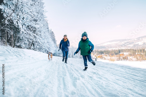 Mother and son having a fun during dog walk. They running with their beagle dog in snowy forest. Mother and son relatives and femily values concept image.