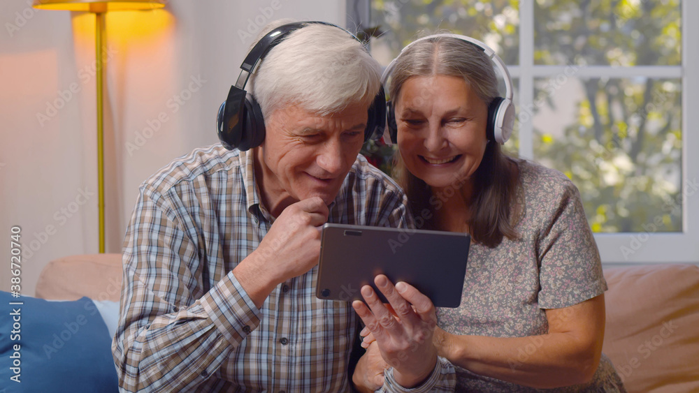 Happy elderly man and woman in headphones watching video on tablet pc at home Happy elderly man and woman in headphones watching video on tablet pc at home