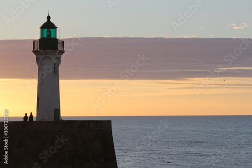 a lighthouse at the normandien coast with the blue sea and orange and purple sky in the background at a summer evening in france