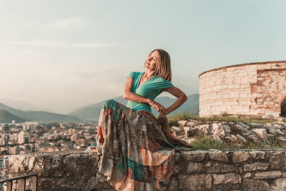 Fototapeta premium Adult woman does sports exercise. Yoga teacher doing an asana on the old city wall.