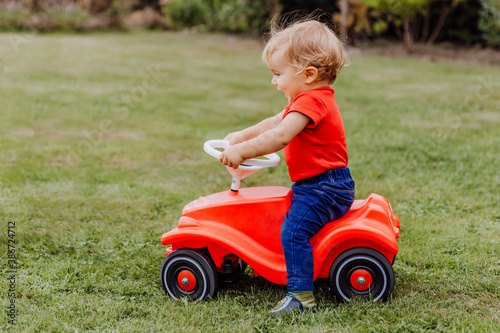 Baby girl riding toy car in garden