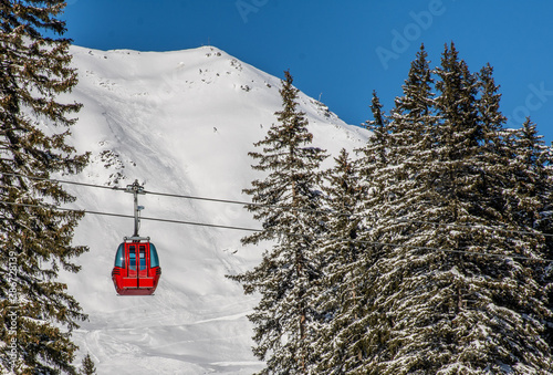 
red ski lift gondola between the fir trees on a background of snowy mountains photo