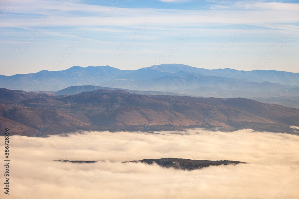 Hill raising above the thick fog covered by forest and distant, impressive horizon mountains