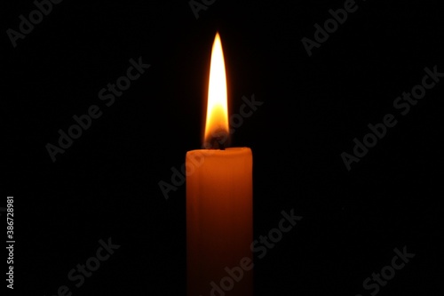 Gelblich leuchtende Kerze brennt in der Nacht vor schwarzem Hintergrund.