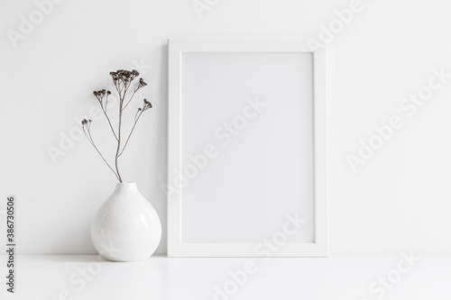 Frame and dry twigs in vase on bookshelf or desk. Mockup.	