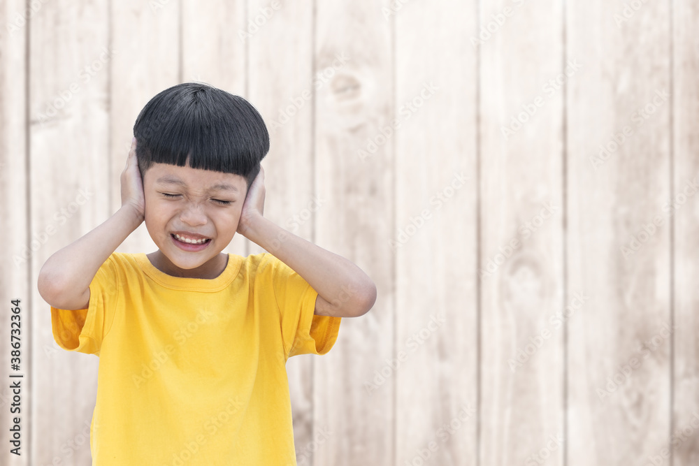 Asian little child covered his ears with wood wall background. Domestic Family violence concept. sad and unhappy child. Asian little child covered his ears with wood wall background. Domestic Family violence concept. sad and unhappy child.