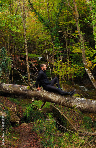 young man sit in to a tree trunk in the forest