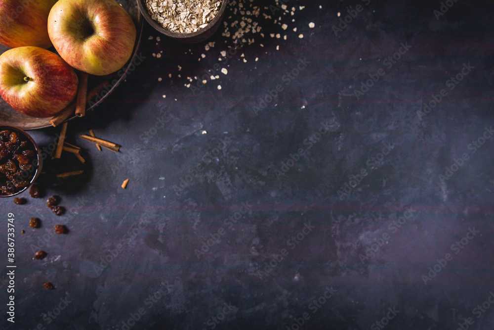 Empty dark concrete background with baking ingredients, Cinnamon, raisins, apples, oatmeal.