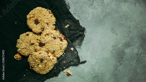 Freshly baked apple, oatmeal, rainsin, cinnamon and nuts cookies with ingredients on a green concrete surface and a dark green cheesecloth. Room for text.