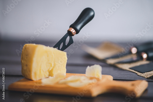 Composed cloesup detail view of aged cheddar cheese with cheese knife set, over vintage brown wooden backdrop