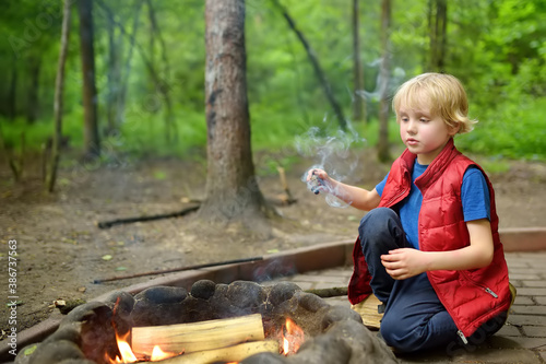 Little boy during family hiking plays with a burning stick by the bonfire. Child having fun at camp fire. photo