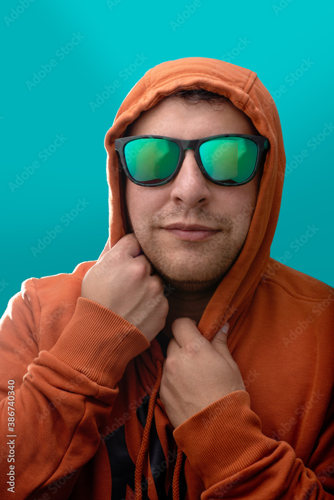 Hombre joven con sudadera naranja gafas oscuras en fondo azul turquesa  Stock Photo