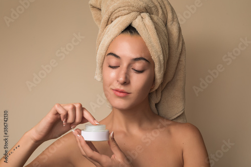 Joven Mujer mexicana con toalla en la cabeza mostrando crema facial humectante producto de belleza photo