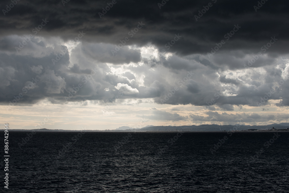 Mer et ciel nuageux très sombres et contrastés avant l'orage avec au loin vue sur la côte