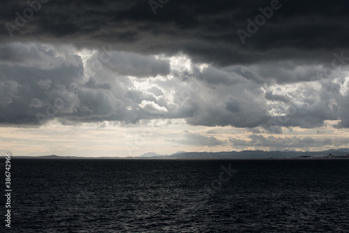 Mer et ciel nuageux très sombres et contrastés avant l'orage avec au loin vue sur la côte