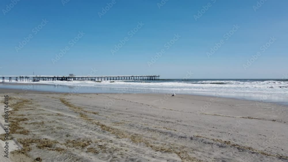 Rough ocean with large waves crashing on the sandy beach and long pier in the distance Rough ocean with large waves crashing on the sandy beach and long pier in the distance