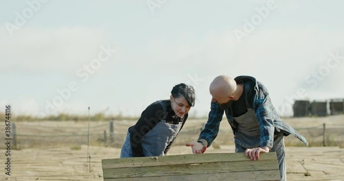 Farmer explaining the breeding of snails to a young woman in dungarees on a windy day on a snail farm. Portrait of a handsome farmer standing in front of the hothouse farm with snail breeding