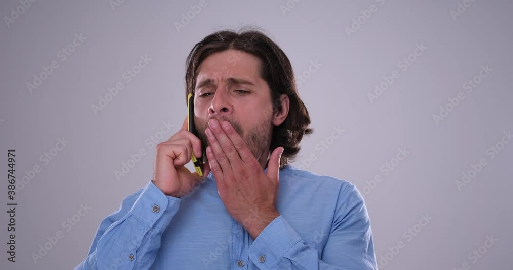 Bored man yawning and fed up of irritating gossip on mobile phone call