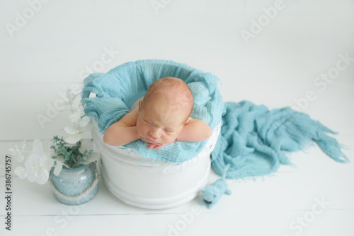 A one week old newborn baby girl sleeping in a little, wooden bucket. She is wearing a cream colored bow headband. Shot in the studio on a white background.newborn photoshoot