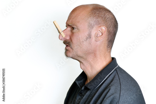 Profile of grimacing man with a clothes pin on nose
